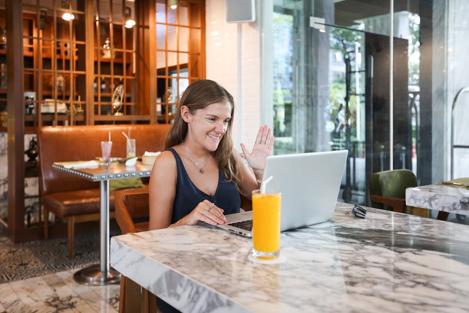 Young woman smiling while working on a laptop in a busy coffee shop