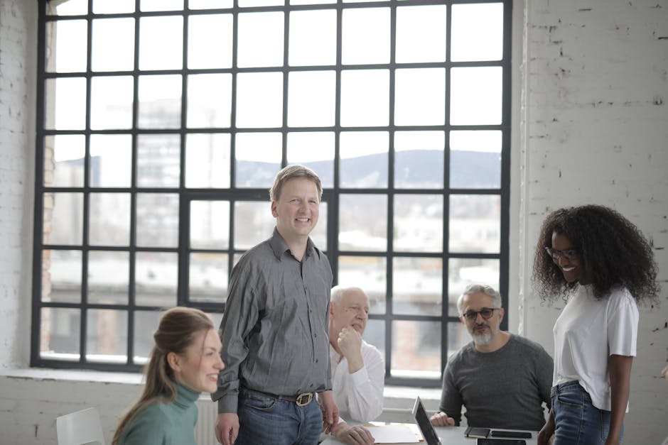 Remote workers smile around a laptop in a bright coworking space.