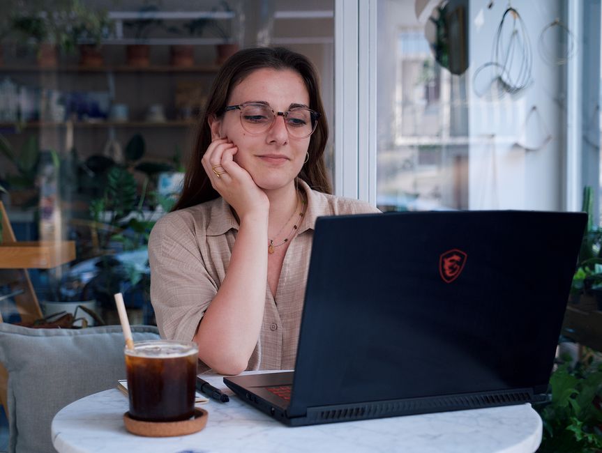 A young woman sitting in a coffee shop looking tired beside her laptop